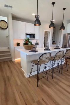 a large kitchen with white cabinets and wooden flooring, along with bar stools