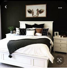 a bedroom with black walls and white bedding is pictured in this image, there are two nightstands on either side of the bed