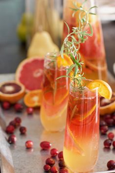 two glasses filled with drinks and garnished with orange slices, cranberries and rosemary