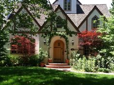 a house that is surrounded by trees and bushes in front of the door, with steps leading up to it