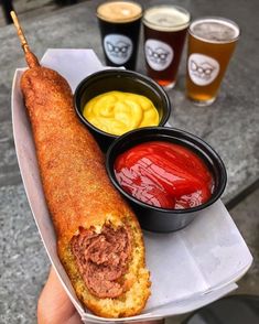 a person holding a long sandwich with sauces and ketchup on the side