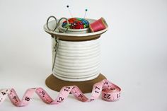 Oversized spool shaped lidded container for sewing implements. Scissors stored in compartment, pincushion topper and bobbin and sewing notion storage. Pink measuring tape coiled and ready to use Sewing Machine Table, Storage Decor