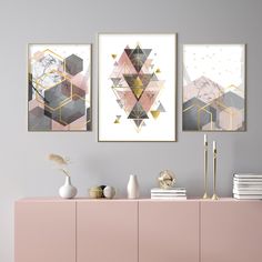 three abstract paintings hang on the wall next to a pink cabinet and white vases