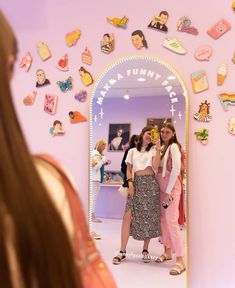 two girls standing in front of a mirror with magnets on the wall behind them