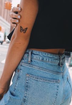 a woman with a small butterfly tattoo on her left arm and right hand behind her back