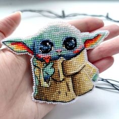 a hand holding a small cross stitched star wars baby yoda