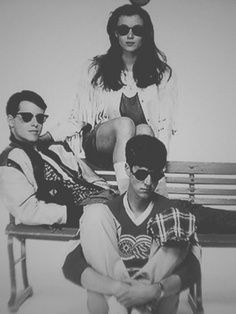 three people sitting on a bench with one person wearing sunglasses and the other looking at the camera