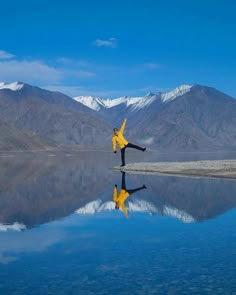 a woman in yellow jacket doing yoga on the beach next to water with mountains in background