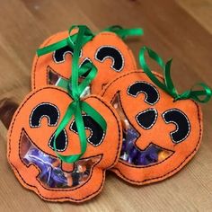 three orange pumpkin shaped candy bags tied with green ribbon on top of a wooden table