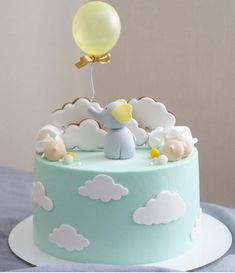 a blue and white cake topped with a yellow balloon flying over clouds on top of it