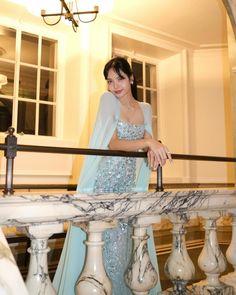 a woman in a blue and white dress standing on a balcony with her hand on the railing