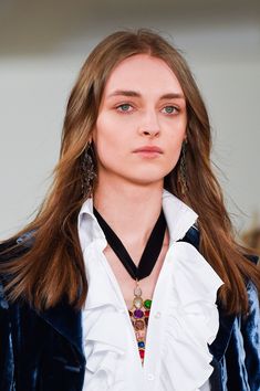 a woman with long hair wearing a white shirt and blue jacket on the catwalk