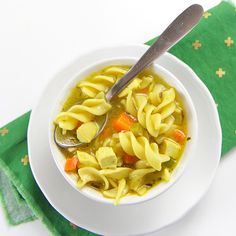 a white bowl filled with noodles and carrots on top of a green napkin next to a spoon