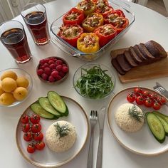 a white table topped with plates of food and veggies next to glasses of juice