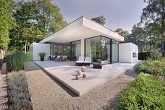 a modern house in the middle of some trees and bushes, with an open patio area