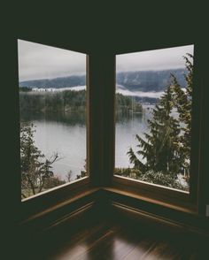 two windows with the view of a lake and trees outside them, in a dark room