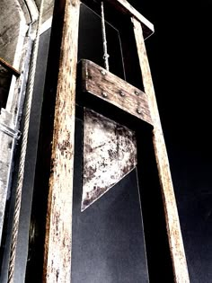 an old wooden sign hanging from the side of a tall building next to a window