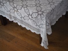 a white table cloth with an intricate design on the top and bottom, sitting on a wooden floor