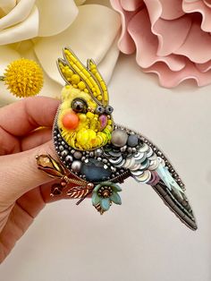 a bird brooch sitting on top of a person's hand next to flowers