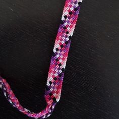 a pink, purple and white beaded lanyard on a black table with a silver clasp