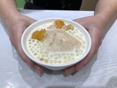 a person holding a white bowl filled with liquid and fruit toppings on top of it