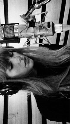 a woman with long hair standing in front of a microphone and headphones on top of her head