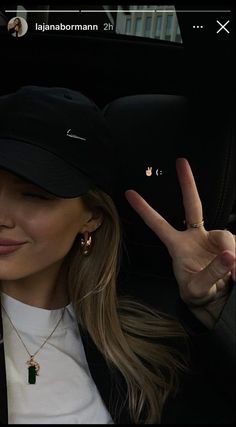 a woman in a car making the peace sign with her hand and wearing a black hat