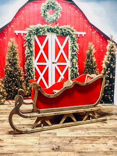 a red sleigh sitting in front of a barn with christmas decorations on it