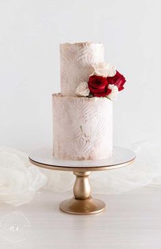 a three tiered wedding cake with red and white flowers on the top is sitting on a gold plate