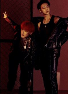 two young men standing next to each other in front of a red wall and fence