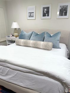 a white bed with blue pillows and pictures on the wall above it in a bedroom