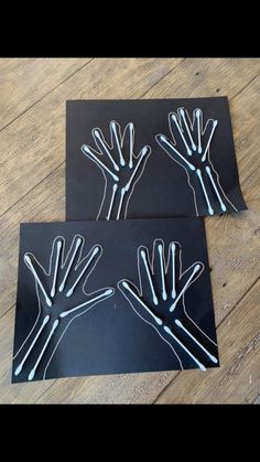 two pieces of black paper with white hand prints on them