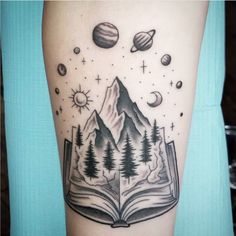 an open book with mountains, trees and planets on it is shown in front of a woman's arm