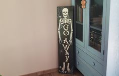 a tall wooden sign with a skeleton painted on it in front of a blue cabinet