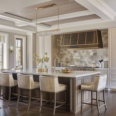 a large kitchen with an island in the middle and several chairs around it, along with two windows