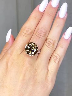 a woman's hand with white nails and a ring on her finger, holding an oval shaped diamond