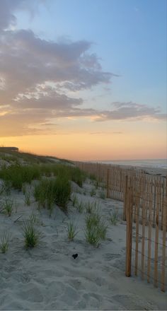 the sun is setting at the beach with tall grass and fence posts in the foreground