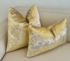 two gold pillows sitting on top of a white couch