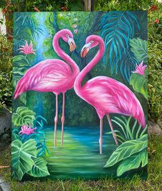 two pink flamingos standing next to each other in front of some plants and flowers