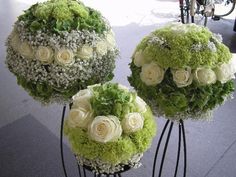 three white roses and green hydrangeas are arranged on black metal stands in front of a sidewalk