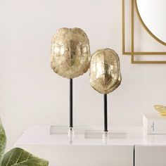 two gold vases sitting on top of a white table next to a mirror and plant