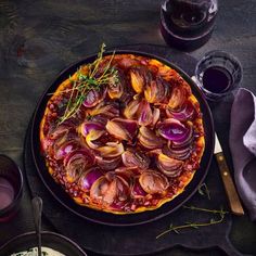 a pizza topped with onions on top of a black plate next to glasses and utensils