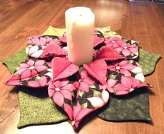 a candle is sitting on top of a table with some fabric flowers and leaves around it