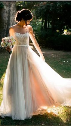 a woman in a wedding dress is walking through the grass with her bouquet on her hand