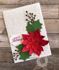 a christmas card with poinsettis and holly on the front, sitting on a wooden surface