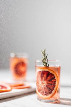 an orange slice in a glass with rosemary garnish on the rim and another plate behind it