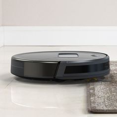 a robotic vacuum on the floor in front of a gray rug and white wall behind it