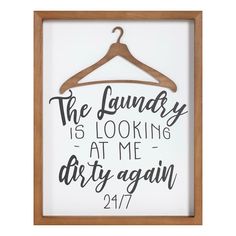 the laundry is looking at me dirty again sign on a wooden frame with clothes hanger