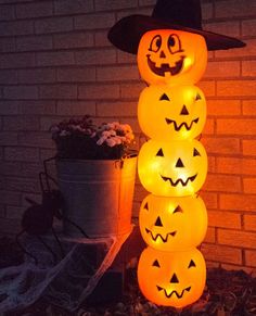 lighted pumpkins stacked on top of each other in front of a brick wall and potted plant