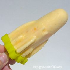 a hand is holding a yellow plastic object that looks like a piece of fruit or vegetable